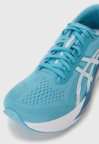 Light blue running shoe featuring a knitted upper, a textured surface, and white accents. The design includes ventilation holes and sturdy laces.