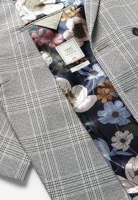 Blazer grigio a quadri con esterno testurizzato. Foderato con un motivo floreale scuro caratterizzato da vari colori. Vestibilità slim, etichettato con taglia 40R.