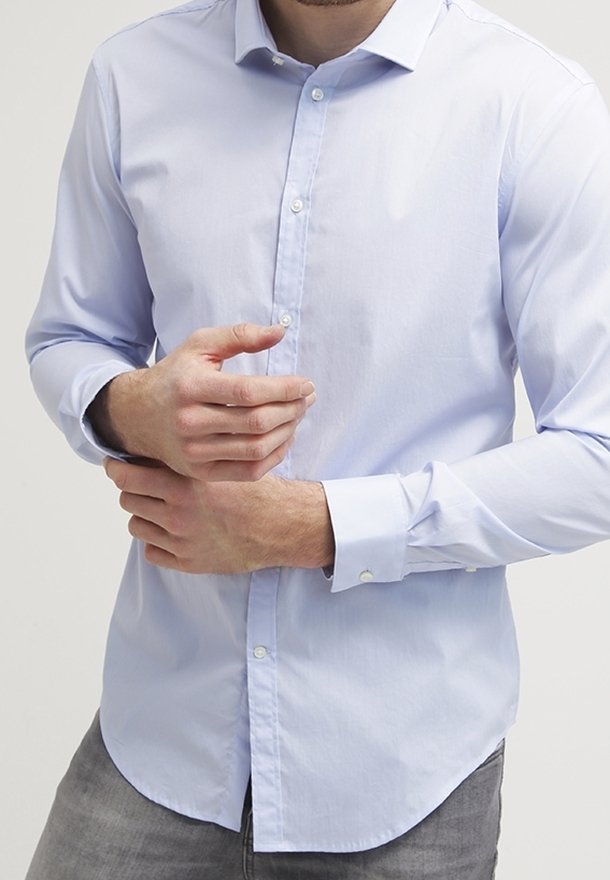 Camicia button-up azzurro chiaro a maniche lunghe in tessuto liscio, con colletto a punta e orlo arrotondato. Presenta bottoni bianchi lungo la parte anteriore.
