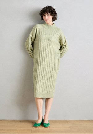 Hellgrünes, gestreiftes Strickkleid mit hohem Kragen und überschnittenen Ärmeln, das knapp über dem Knie endet. Kombiniert mit grünen Ballerinas.