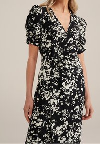 Černé květinové šaty s bílými abstraktními květy, s nabíranými rukávy, výstřihem do V a uzlovým detailem v pase. Texturovaná tkanina.