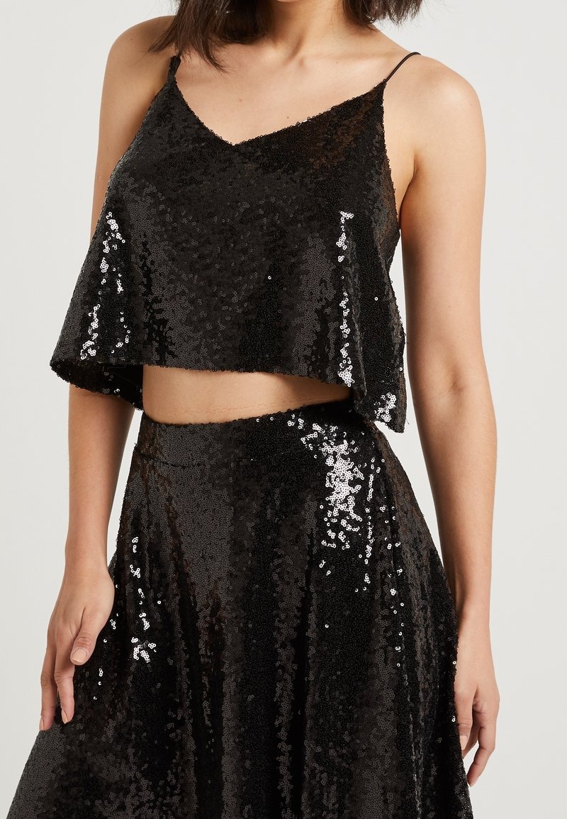 Black sequined crop top with a V-neckline and spaghetti straps. Flowy design with an exposed midriff, featuring shimmering, textured surface.