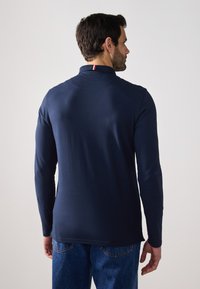 Polo de manga larga en color navy con cuello, que cuenta con un pequeño acento en rojo y blanco en el cuello. Fabricado en una tela suave y elástica.