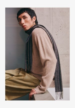 Beige knit sweater with a high neck, paired with olive green wide-leg pants. A striped dark gray scarf drapes over the shoulder.