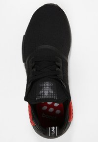 Svart träningsskor med en texturerad stickad ovandel, svarta snörningar, röda accenter på hälen och en mönstrad innersula som har ordet "boost".