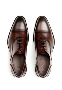 Chaussures habillées en cuir marron avec une finition brillante, bouts pointus et détails de couture subtils. Elles présentent un laçage sur le devant et une texture lisse.