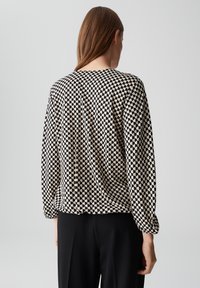 Langarmshirt mit einem schwarzen und beigen Schachbrettmuster, lockerer Schnitt und weichem Stoff, ergänzt durch einen runden Halsausschnitt.