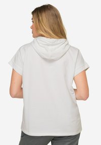Camiseta blanca con capucha y mangas cortas, hecha de una tela suave. Presenta un diseño sencillo e incluye una capucha en la parte trasera.