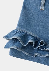 Ourlet de jupe en denim avec bords à volants superposés et détail de couture visible dans un tissu bleu sur un fond uni.