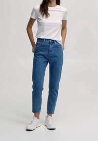 White short-sleeve t-shirt paired with high-waisted blue jeans. Jeans have a straight leg and cropped hem. White sneakers complete the outfit.