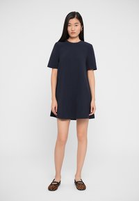 Navy blue shift dress with short sleeves, round neckline, and a loose fit. Features smooth fabric and a minimal design, worn with patterned flats.