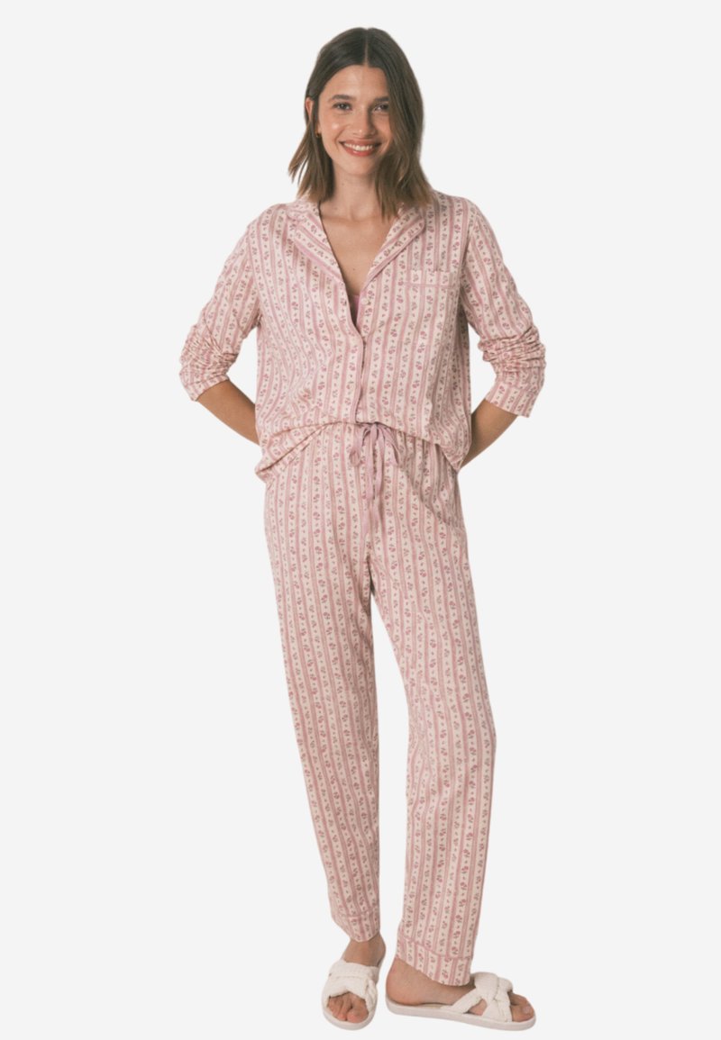 Růžový vzorovaný pyžamový set, který obsahuje košili na knoflíky s náprsní kapsou a kalhoty se stahovací šňůrkou. Měkká tkanina a volný střih. Včetně pantoflí.