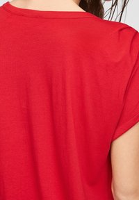 Maglietta a maniche corte, con collo a giro, in cotone rosso brillante. Tessuto liscio con vestibilità casual, presenta un dettaglio di cucitura pulita sulla spalla.