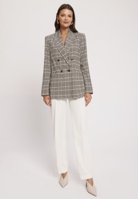 Podwójnie zapinana marynarka w kratę w beżowo-czarnym kolorze, z dopasowanym krojem, długimi rękawami i klapami w kształcie litery V, zestawiona z białymi spodniami.