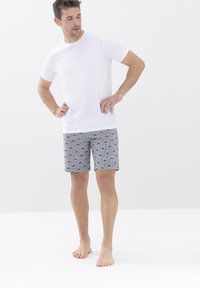 Camiseta blanca de manga corta combinada con pantalones cortos grises de patrones que presentan diseños circulares en verde y negro sobre un fondo a rayas.