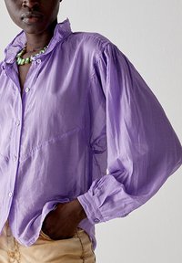 Camicia oversize viola con colletto rialzato, maniche rilassate e tessuto leggero e leggermente trasparente. Polsini regolabili.