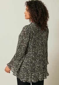Blouse noire et crème à motif avec un design plissé, des manches évasées et un ourlet à vagues, fabriquée dans un tissu léger et texturé.