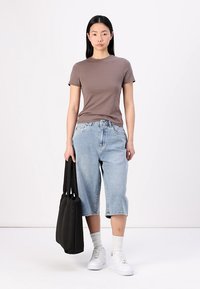Camiseta de algodón marrón combinada con culottes de mezclilla de lavado claro. Zapatillas blancas y un bolso tote negro completan el atuendo. Diseño sencillo y casual.