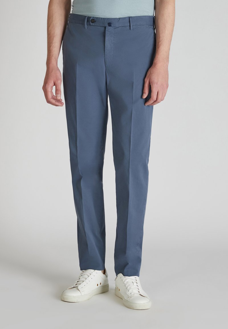 Pantaloni di cotone blu a taglio slim, con frontale piatto, due tasche laterali e chiusura con bottone. Abbinati a sneaker bianche.