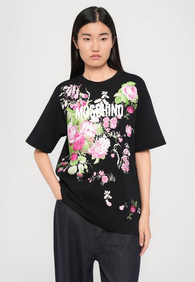 Melna kokvilnas t-kreklu ar spilgtiem ziedu motīviem rozā un zaļā krāsā. Priekšpuses dizainā ir uzraksti "MOSCHINO" un "ANDERSON." Īsas piedurknes.