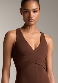 Brun ärmlös klänning med djup V-ringning och korsad design. Tillverkad av ett smidigt material, har en figurnära passform och rena linjer.
