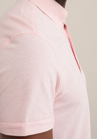 Světle růžové polo tričko s límečkem, krátkými rukávy a strukturovanou tkaninou s jemným prošíváním.