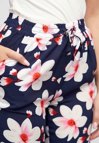 Pantaloni fiorati blu navy con grandi fiori bianchi e rosa, vita elastica con coulisse e tasche laterali.