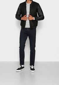 Black bomber jacket with leather sleeves, gray crew neck shirt, dark jeans, and black sneakers with white soles. Minimalist design.