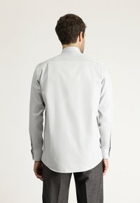 Camicia grigia chiara con maniche lunghe, colletto classico e polsini. Tessuto liscio, con orlo dritto e senza motivi visibili.