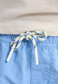 Vaaleansiniset shortsit, joissa on joustava vyötärönauha ja solmittava naru, jonka kuosissa on valkoisia, keltaisia ja sinisiä kuvioita; puuvillakangasta.