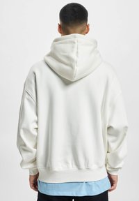 Cream-colored hoodie made of soft fabric, featuring a large hood, dropped shoulders, and a relaxed fit, with a ribbed hem and cuffs.