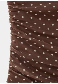 Tissu marron à pois blancs, avec une texture froncée et des coutures rassemblées sur le côté gauche.