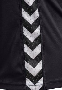 Svart idrottsplagg med en texturerad sidopanel med vita chevronmönster. Designen inkluderar mesh-element och kontrasterande sömmar.