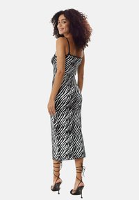 Black and white zebra print midi dress with thin straps, form-fitting design, and textured fabric. Worn with black strappy heels.