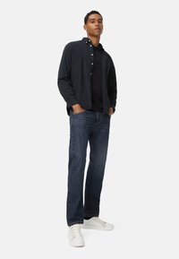 Donker marineblauwe button-down shirt over een zwarte polo, gecombineerd met blauwe jeans en witte sneakers. Glad stof met een casual pasvorm en een klassiek ontwerp.