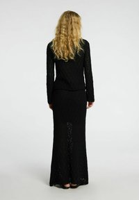 Abito knit nero a maniche lunghe con un motivo testurizzato, caratterizzato da un top aderente e una gonna svasata, indossato con scarpe basse. Visto da dietro.