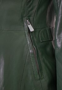 Grüne Lederjacke mit seitlicher Reißverschlusstasche und silbernen Beschlägen sowie einem gesteppten Design. Glatte Textur, maßgeschneiderte Passform.