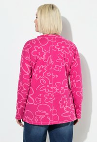 Różowa bluza z nadrukiem kwiatowym na całej powierzchni w jaśniejszym odcieniu różu. Długie rękawy i zaokrąglony dół. Miękki materiał z widocznymi detalami przeszyć.