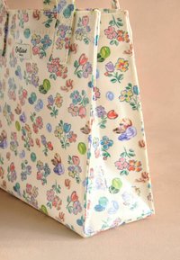 Borsa a mano floreale con sfondo color crema, caratterizzata da motivi di fiori e foglie colorati, realizzata in tessuto strutturato con manici robusti.