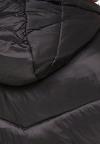 Chaqueta de plumas negra con un diseño acolchado, que presenta una capucha, textura brillante y costuras visibles a lo largo de las costuras y patrones en forma de chevrón.