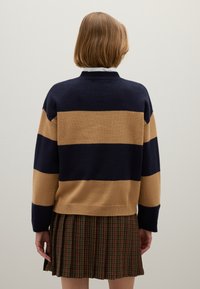 Ein gestrickter Pullover mit horizontalen Streifen in Marineblau und Beige, ausgestattet mit einem gerippten Kragen und Saum, kombiniert mit einem gepließten Karo-Rock.