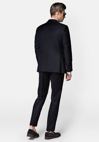 Granatowy garnitur o dopasowanym kroju, z marynarką na dwa guziki i zwężanymi spodniami. Połączenie z butami wsuwanymi dopełnia całość.