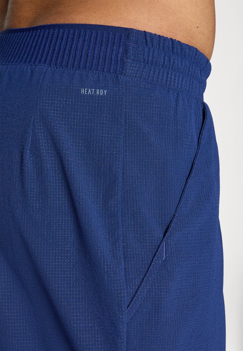 Pantalones cortos deportivos color azul marino con un tejido texturizado, cinturilla de malla y un bolsillo lateral, etiquetados como "HEAT.RDY" cerca de la parte superior.