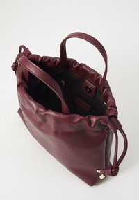 Sac seau en cuir bordeaux avec un dessus froncé, de courtes poignées et des finitions en métal doré. L'intérieur comprend une poche zippée. Texture lisse.