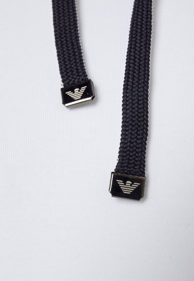 Mustad valmistooted mustad kudumistrapid metalliliste ruudukujuliste aktsentidega, millel on logo. Sile tekstuur ja tugev, vastupidav materjal. Sobib aksessuaaride või rõivaste jaoks.