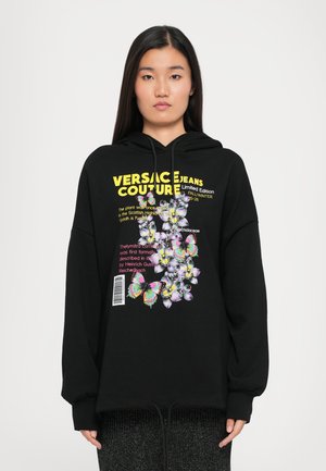 Black hoodie with a front graphic featuring colorful butterflies and floral designs. Text includes "Versace Jeans Couture" and barcode detail.