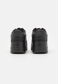 Ein Paar schwarze, klobige PlattformSneaker von hinten auf einem weißen Hintergrund gezeigt.