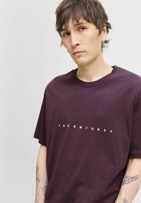 Bordo pamučna majica s okruglim izrezom i bijelim printom "JACK & JONES" na prednjoj strani. Opusti kroj s kratkim rukavima.