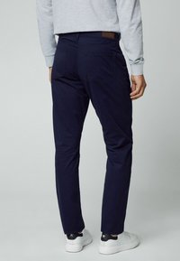 Marineblaue Slim-Fit-Hosen mit glatter Textur, fünf Taschen und einem Lederpatch am Bund, kombiniert mit weißen Sneakern.