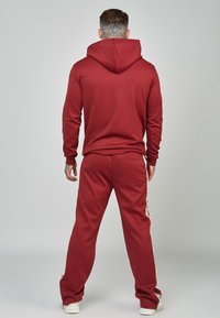 Weinrotes Hoodie- und Jogginganzug-Set; weicher Stoff; tailliertes Design; Hoodie mit großem Halsausschnitt; Hose mit seitlichen Streifen; einfarbige Textur.